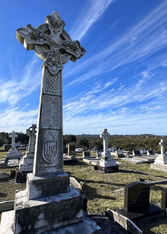 Large celtic cross adorns the gravesite of William Webster surrounded by other graves. 
